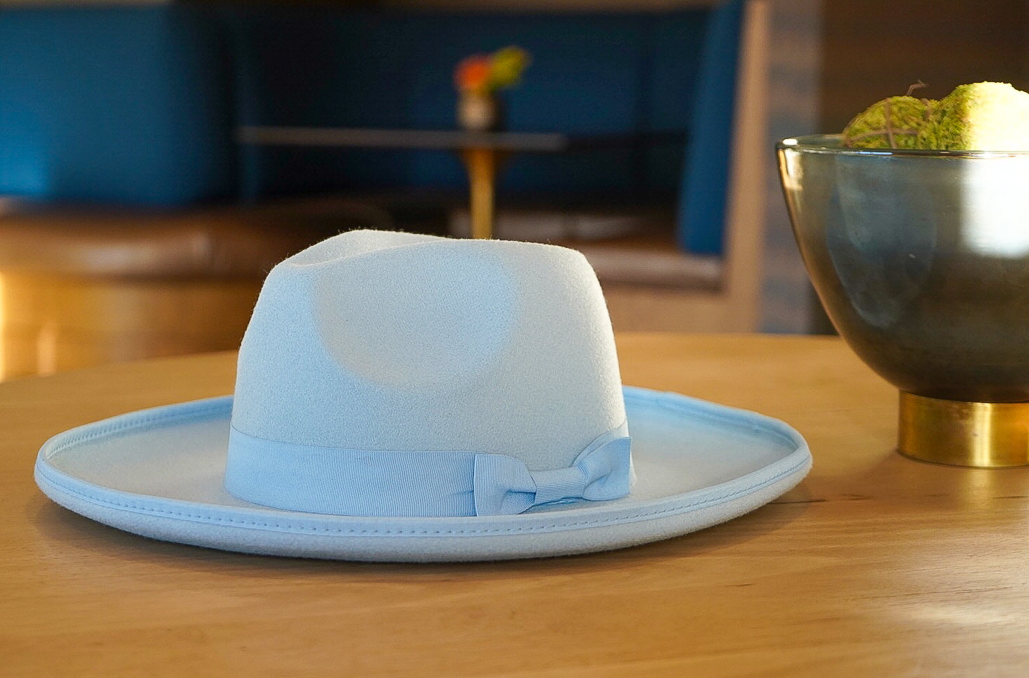Product photo of a sky blue cureled brim fedora with a bowtie.